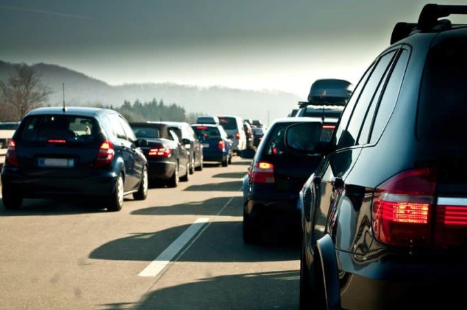 Cars are lined up in heavy traffic on a Michigan highway under a cloudy sky, with distant hills in the background, illustrating the impact of the recent No Fault Reform on drivers' experiences.