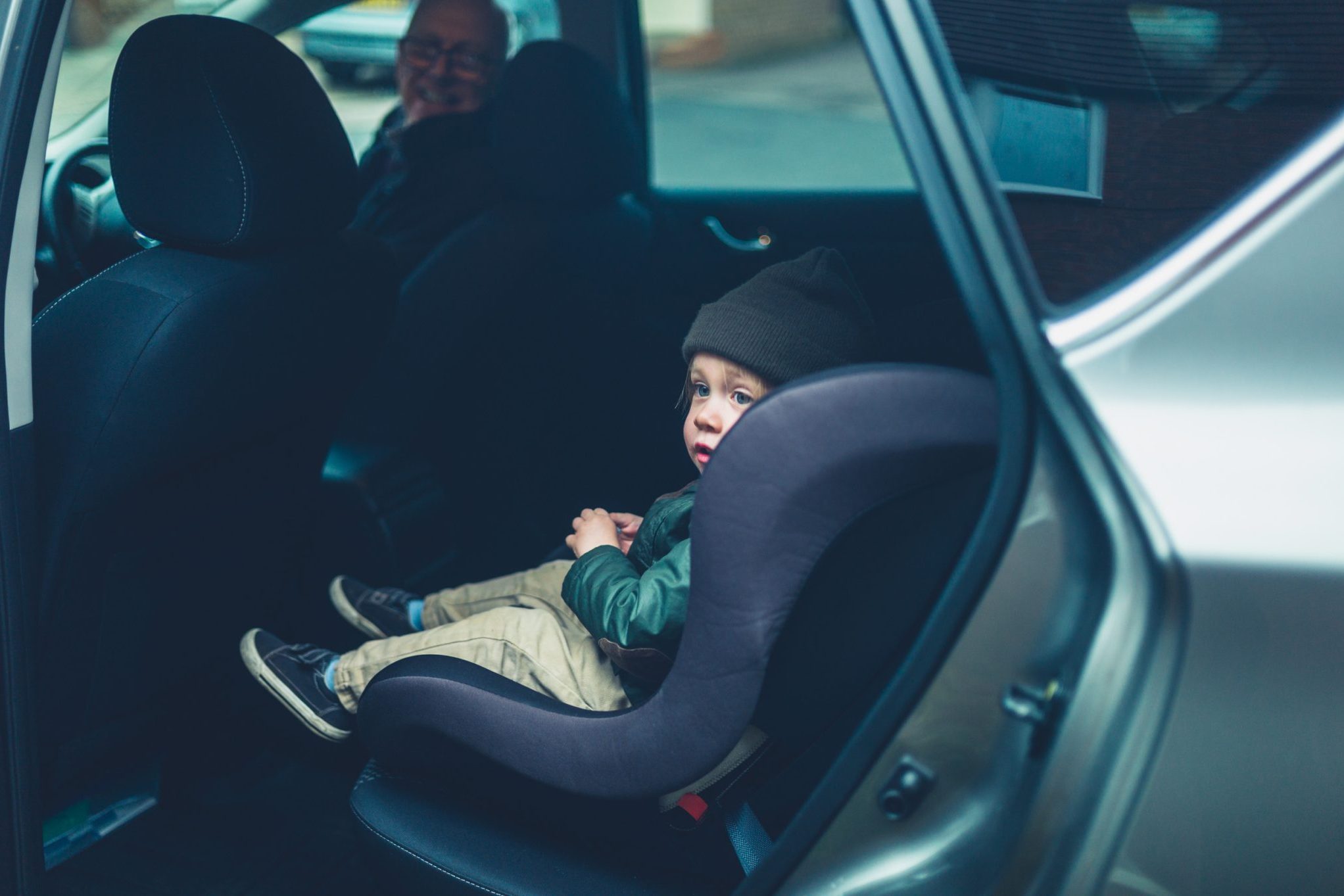 A child is safely seated in a car seat in the back of a vehicle, complying with Michigan Car Seat Laws, while an adult accompanies them from the front seat.