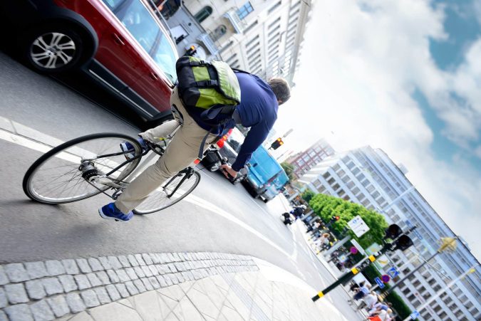 A cyclist rides through the bustling cityscape of Lansing, effortlessly navigating the road amidst a sea of cars.