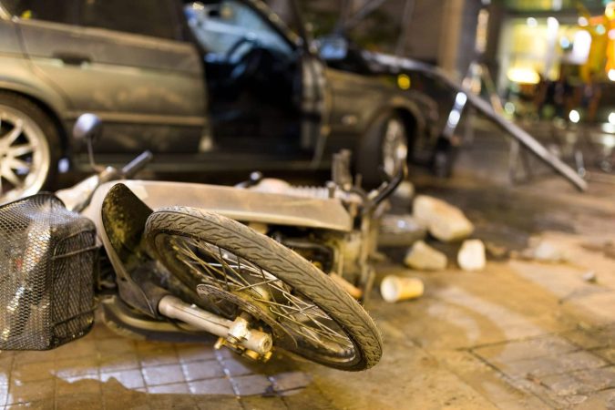 A motorcycle lies overturned on a wet pavement, the aftermath of a motorcycle accident with a damaged car. Debris is scattered around the scene, serving as a stark reminder of the importance of road safety.