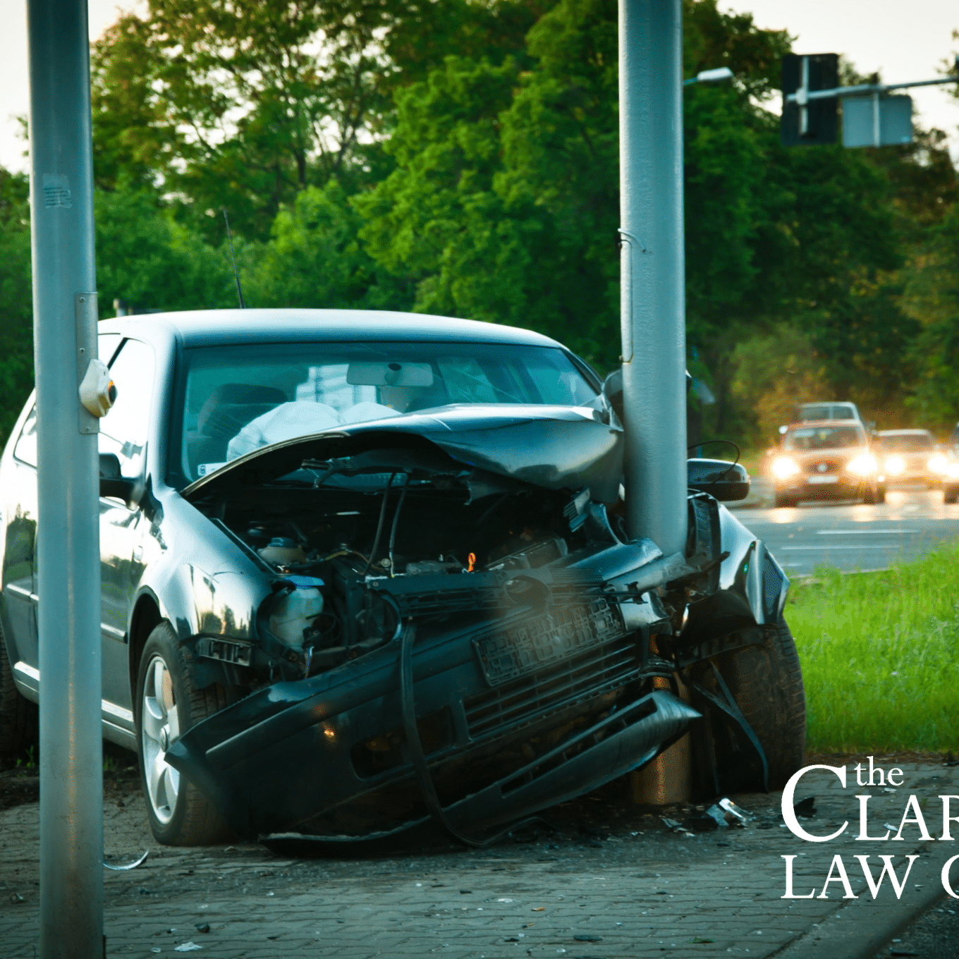 A car crashed head-on into a streetlight pole at an intersection, with front-end damage visible. The Clark Law Office logo is in the image corner.