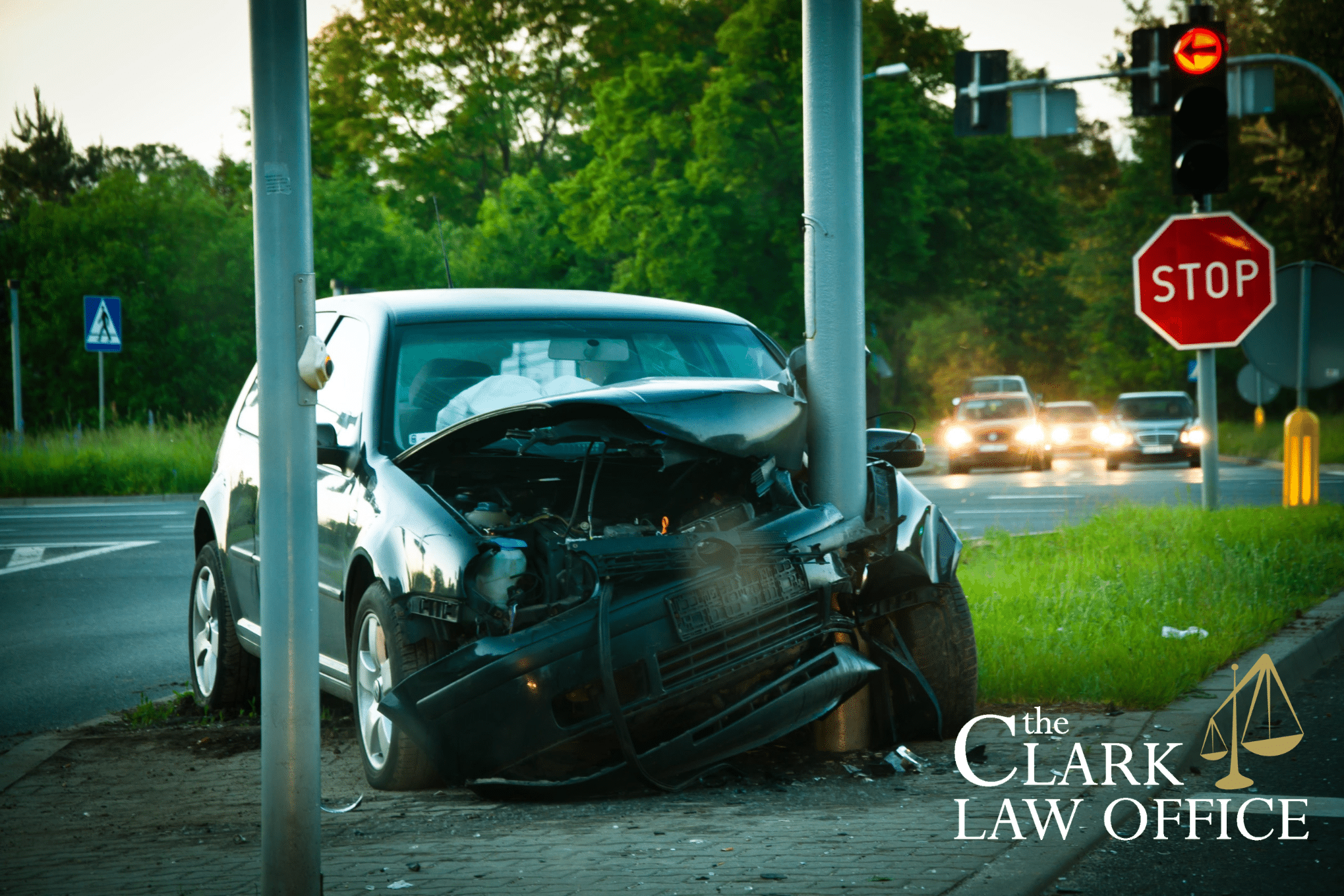 A car crashed head-on into a streetlight pole at an intersection, with front-end damage visible. The Clark Law Office logo is in the image corner.