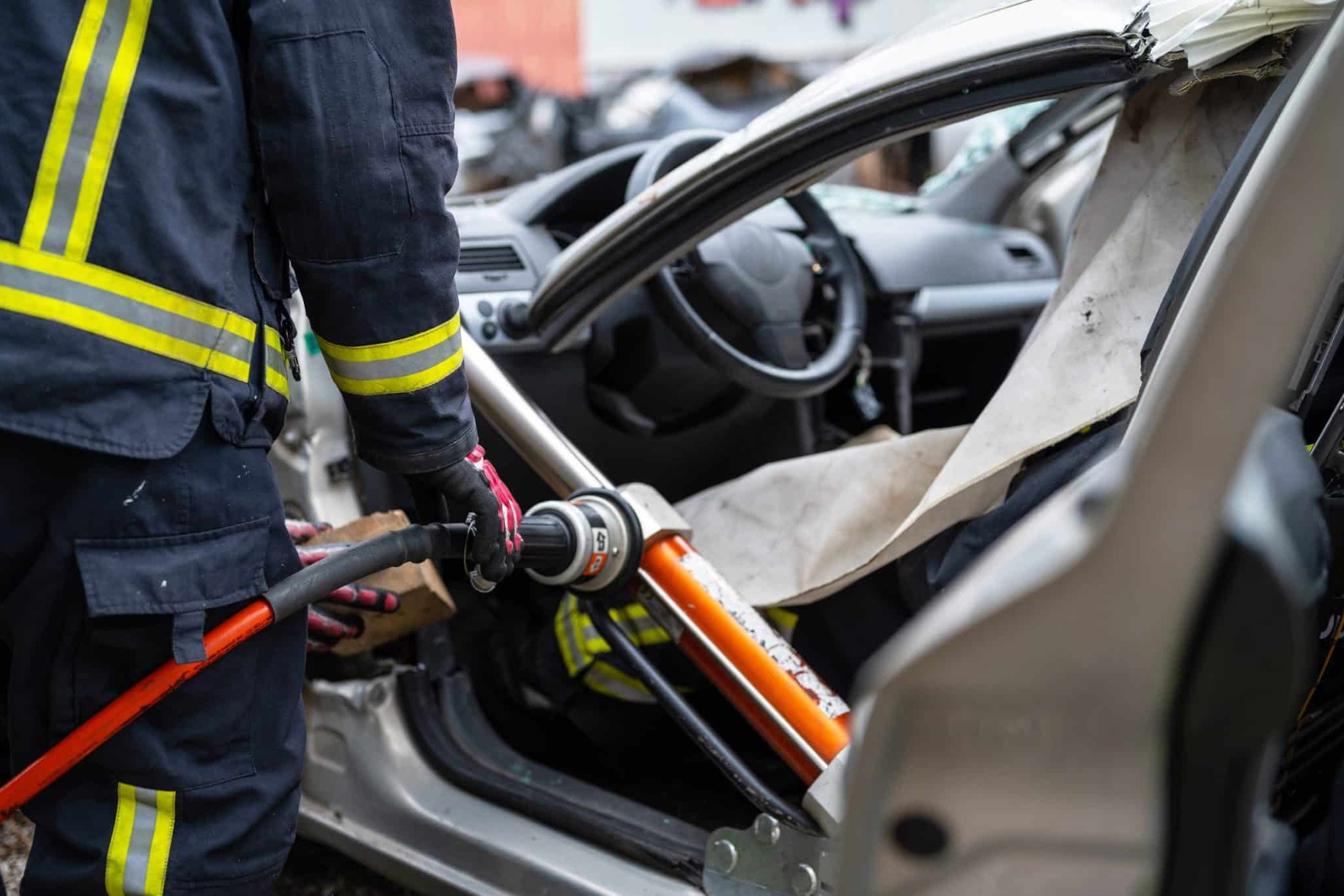 How to prove negligence after a car accident in Lansing In Lansing, a firefighter skillfully uses a hydraulic rescue tool to pry open a damaged car door, granting crucial access to the interior after an accident, often seen in car accident cases linked to negligence.