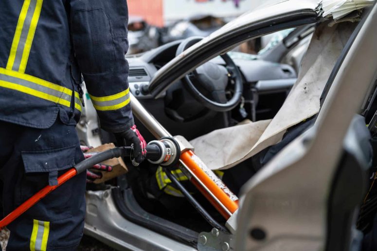 How to prove negligence after a car accident in Lansing In Lansing, a firefighter skillfully uses a hydraulic rescue tool to pry open a damaged car door, granting crucial access to the interior after an accident, often seen in car accident cases linked to negligence.