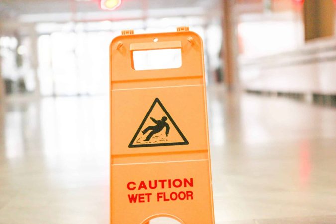 A bright orange "Caution Wet Floor" sign stands on the glossy surface, hinting at the possibility of a slip and fall accident in bustling Lansing's busy establishments. The blurred background adds a sense of urgency, reminding everyone to tread carefully.