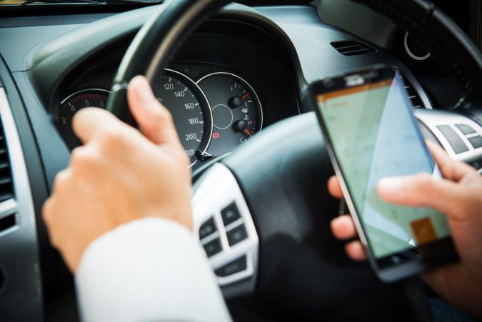 A driver in Lansing, clutching a smartphone in one hand and steering with the other, exemplifies classic distracted driving behavior—a risky action that often leads to accidents.