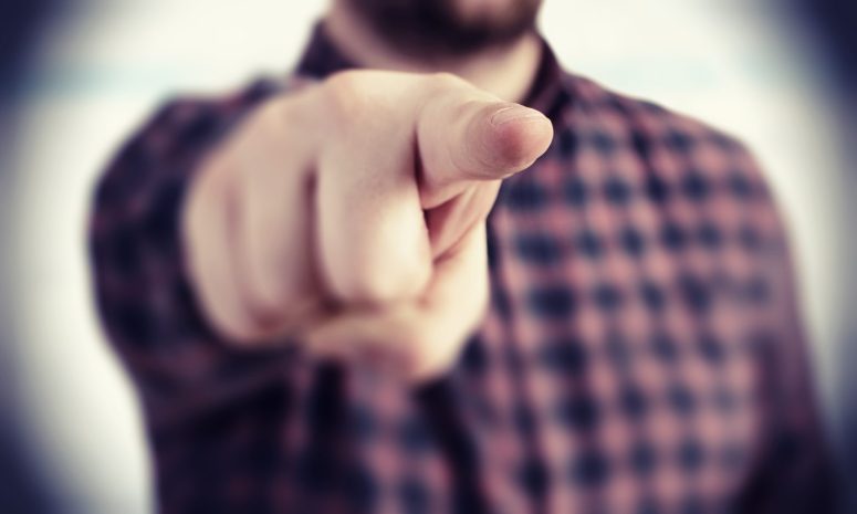 How Comparative Negligence Affects Lansing Car Accident Cases A person in a checkered shirt points their finger directly at the viewer, as if making a claim, with the background artfully blurred.