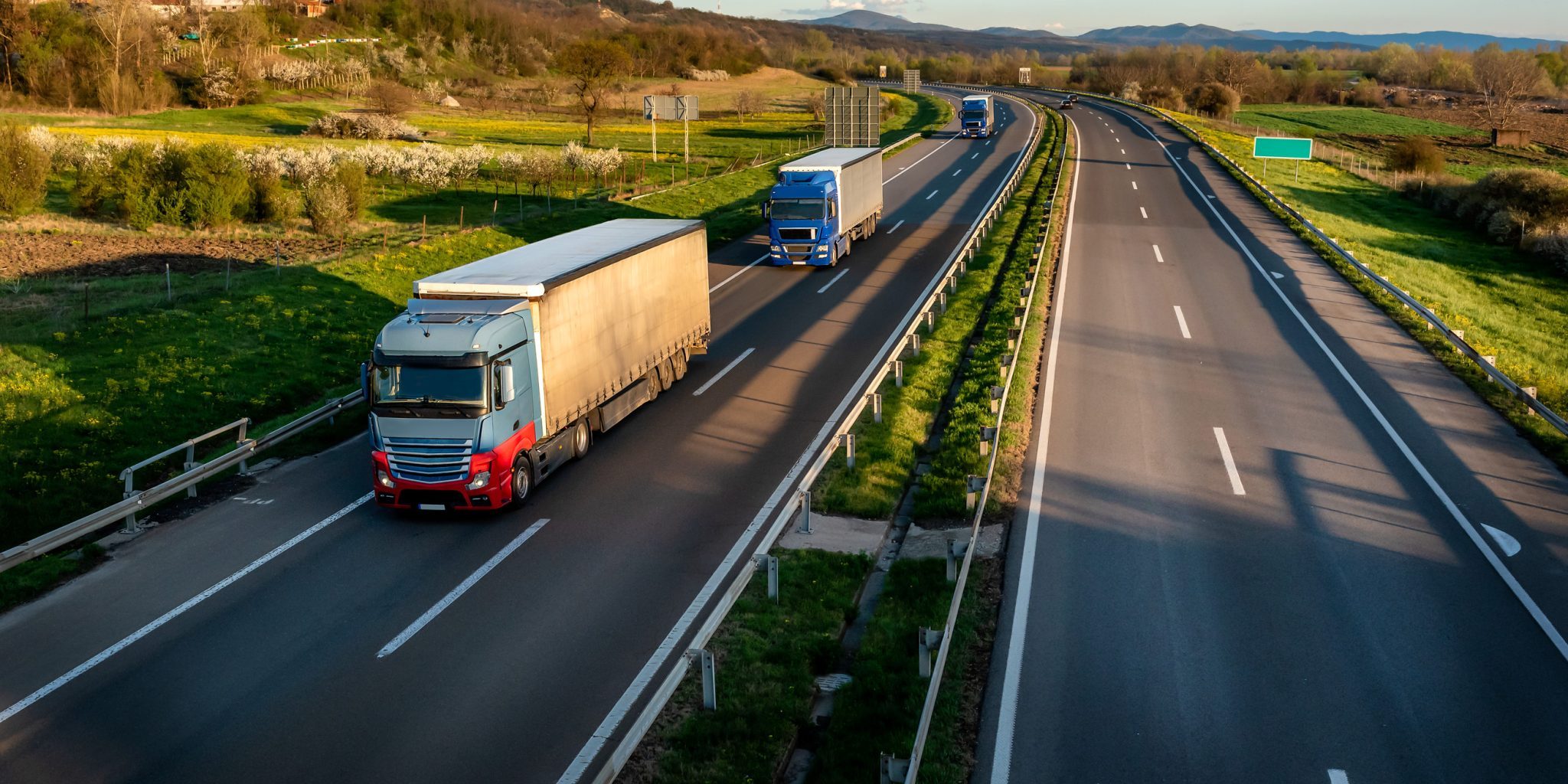 The Most Dangerous Roads for Truck Accidents in Lansing Two trucks journey on a divided highway near Lansing, flanked by green fields and rolling hills under a clear sky.