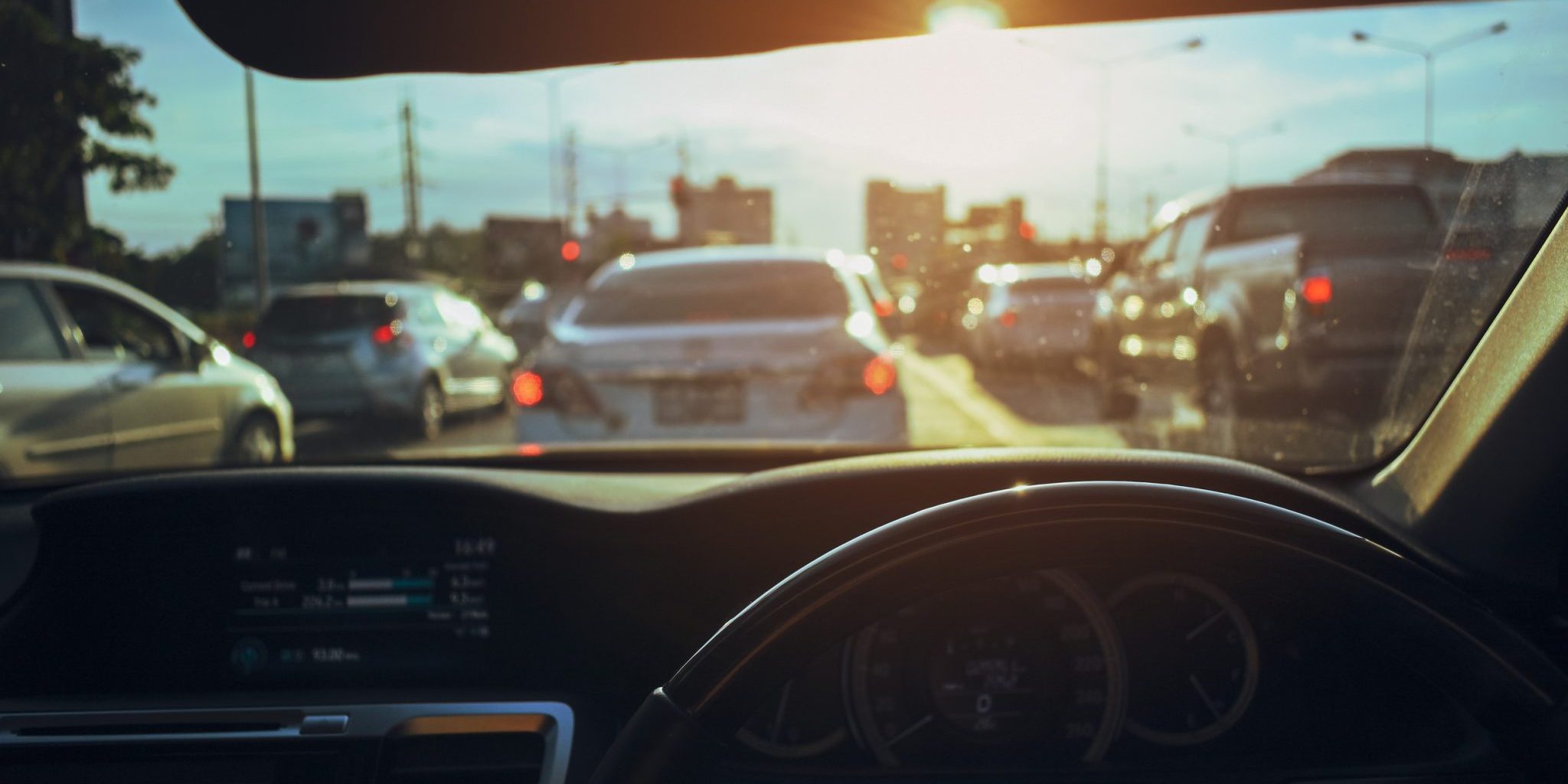 Why Student Drivers Make Lansing’s College Campuses a Hotspot for Car Accidents View from inside a car as student drivers navigate a busy road under bright sunlight, with cars stopped at a traffic light ahead.