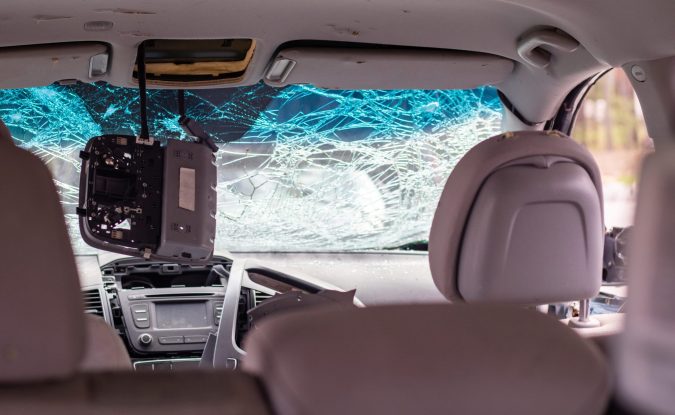 The interior of the car reveals a shattered windshield and a detached rearview mirror hanging down, a vivid reminder of why uninsured motorist coverage is essential in places like Lansing.
