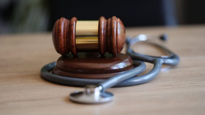 A wooden gavel rests on a sound block with a stethoscope wrapped around it, symbolizing the process to report medical malpractice in Lansing, Michigan, all placed on a wooden surface.