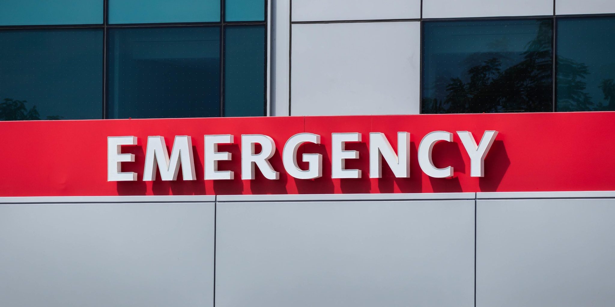 A building exterior sign with bold white letters spelling "EMERGENCY" on a red background, indicating the emergency department at McLaren Lansing hospital.