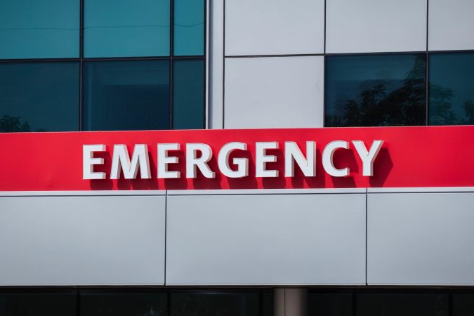 A building exterior sign with bold white letters spelling "EMERGENCY" on a red background, indicating the emergency department at McLaren Lansing hospital.
