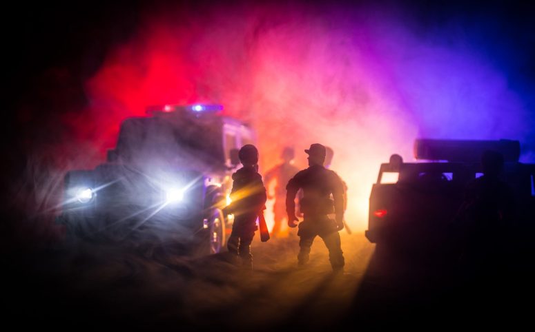 The Investigation Process for Motorcycle, Car, and Truck Accidents in Lansing Silhouettes of toy action figures stand defiantly in front of toy police vehicles with headlights cutting through the red and blue mist, evoking the chaotic aftermath of car accidents.