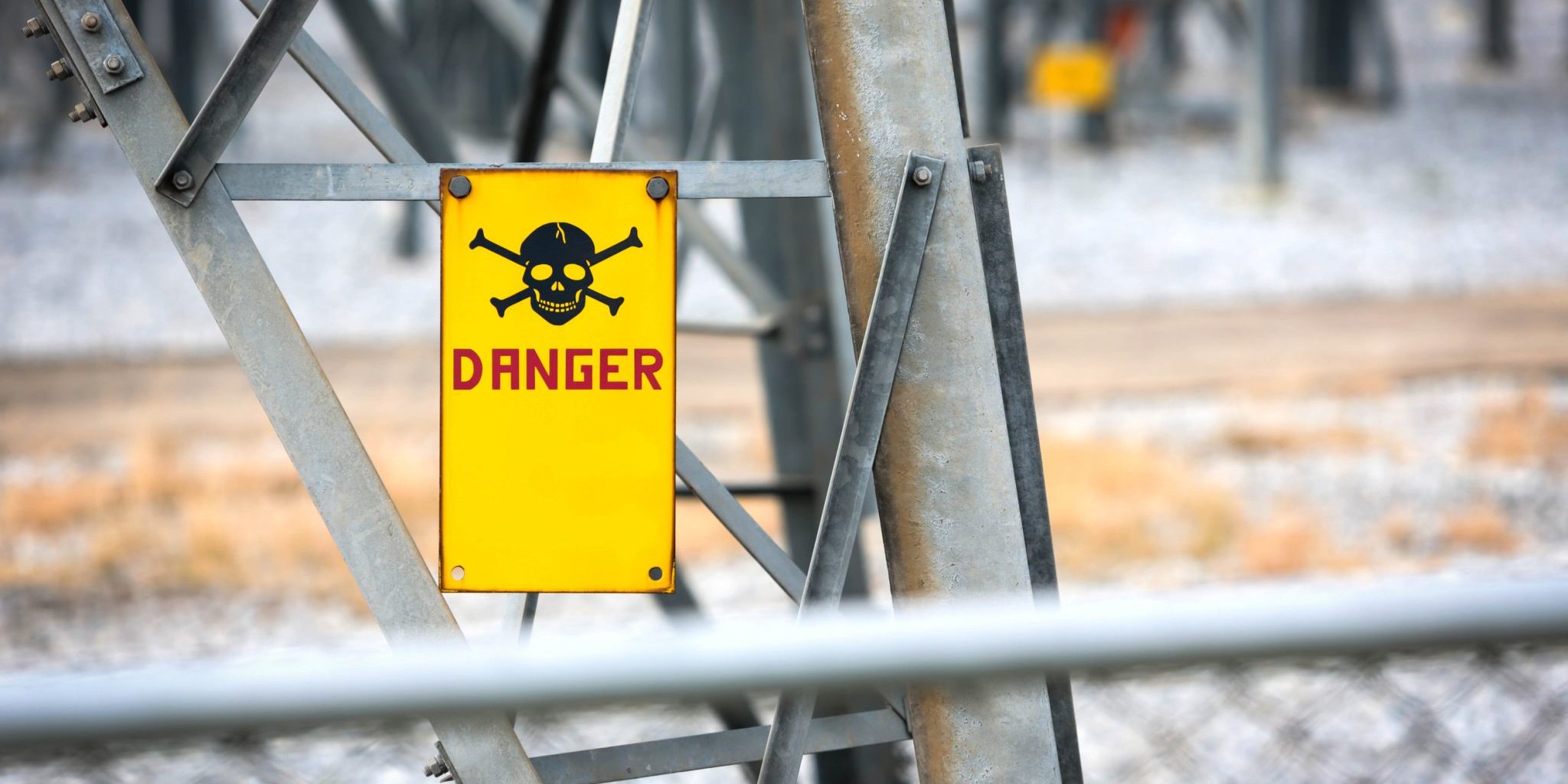 Yellow "Danger" sign with skull and crossbones attached to a metal structure, warning of hazardous area near power equipment—typical of high-risk places Lansing residents should be aware of, as highlighted in any personal injury guide.