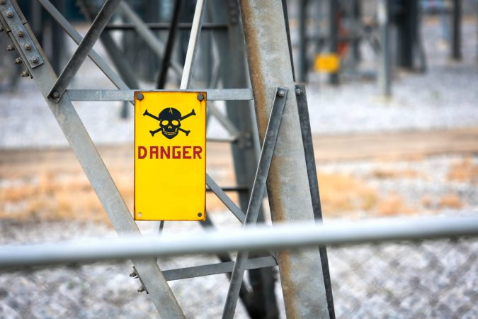 Yellow "Danger" sign with skull and crossbones attached to a metal structure, warning of hazardous area near power equipment—typical of high-risk places Lansing residents should be aware of, as highlighted in any personal injury guide.