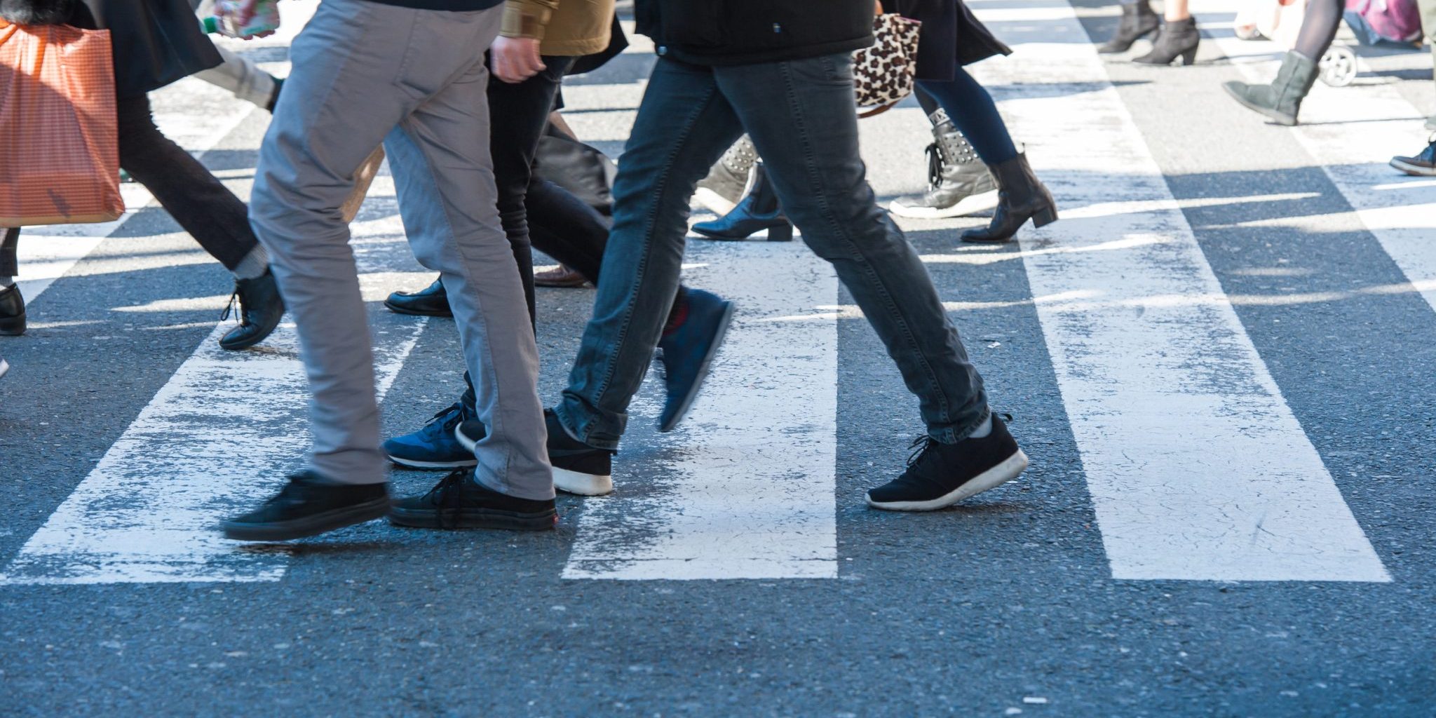 Your Rights After a Pedestrian Accident at MSU or in Lansing People walking across a crosswalk on a city street in Lansing, visible from the knees down, with various shoes and clothing styles—a common scene near MSU and a reminder to stay alert for pedestrian accidents.