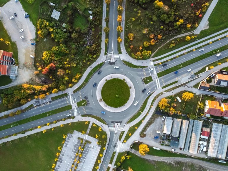 Aerial view of a large roundabout with multiple roads converging in Lansing, highlighting how Lansing roundabouts manage traffic dangers amid green areas, cars, and nearby buildings while promoting driving safety.