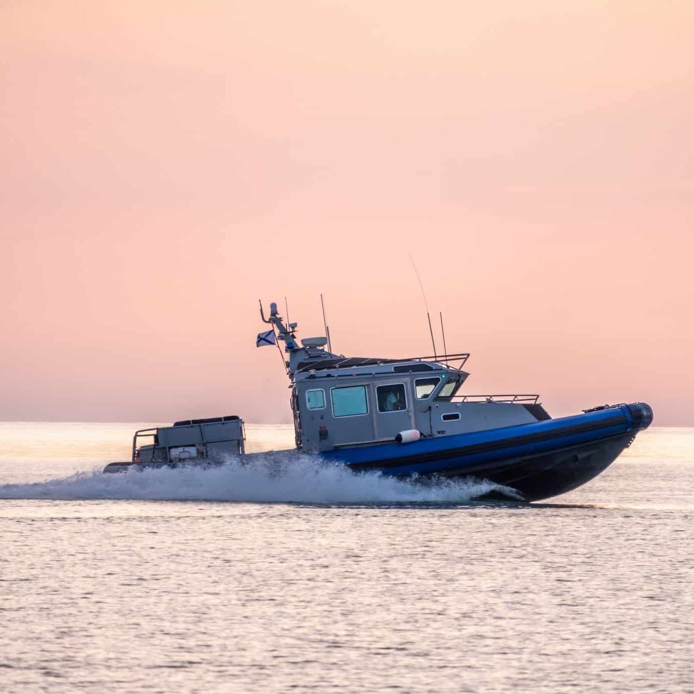 Why Michigan Boaters Keep Making the Same Deadly Mistakes A patrol boat moves quickly across calm water at sunset, creating a trail of spray behind it under a pink and orange sky—a vivid reminder to Michigan boaters to avoid deadly mistakes while enjoying serene evenings.