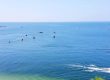 Several boats float on a calm blue Michigan sea under a clear sky, with two people riding a jet ski near the shoreline.