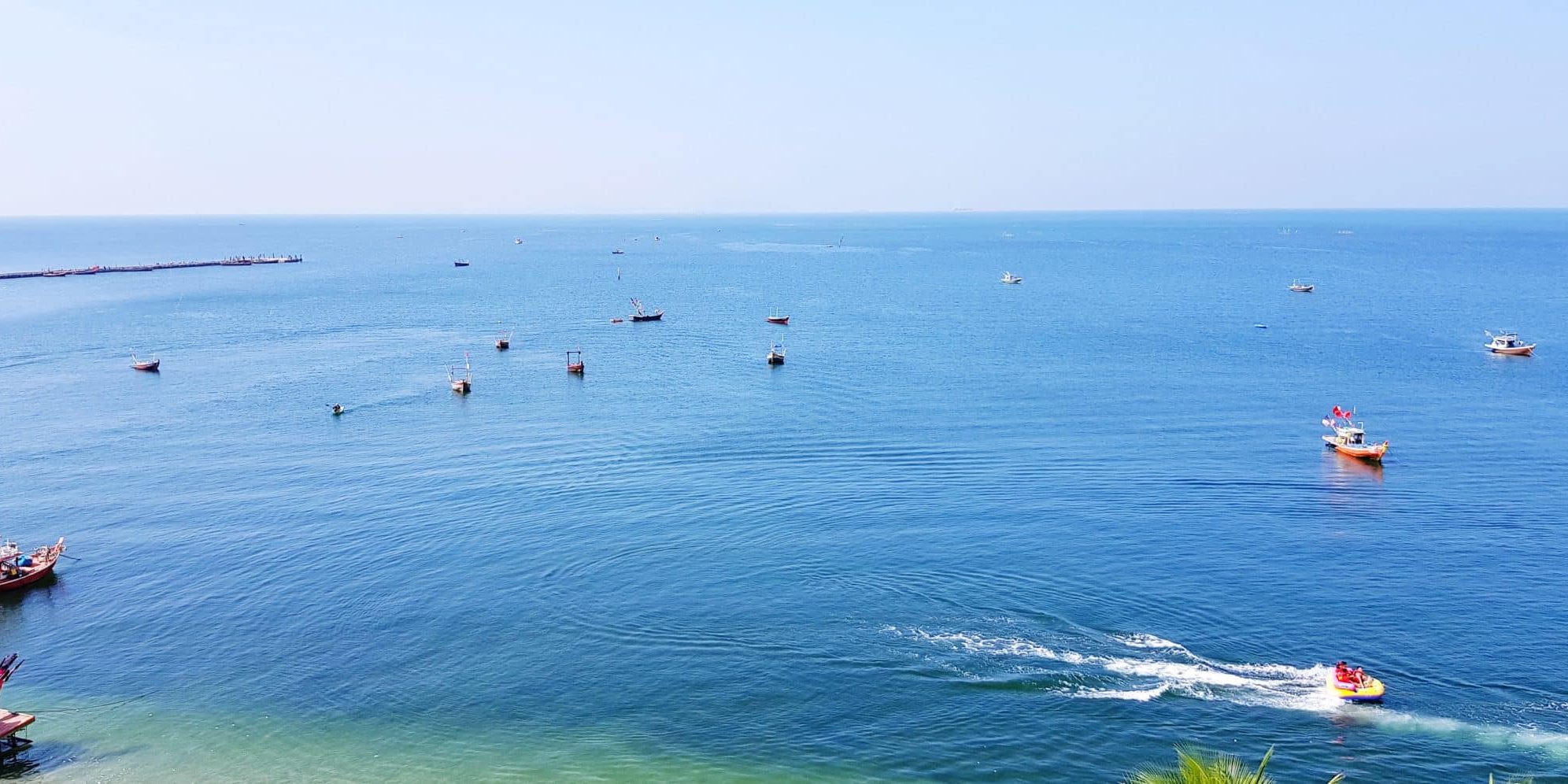 michigan marijuana and boating Several boats float on a calm blue Michigan sea under a clear sky, with two people riding a jet ski near the shoreline.