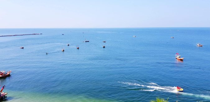 michigan marijuana and boating Several boats float on a calm blue Michigan sea under a clear sky, with two people riding a jet ski near the shoreline.