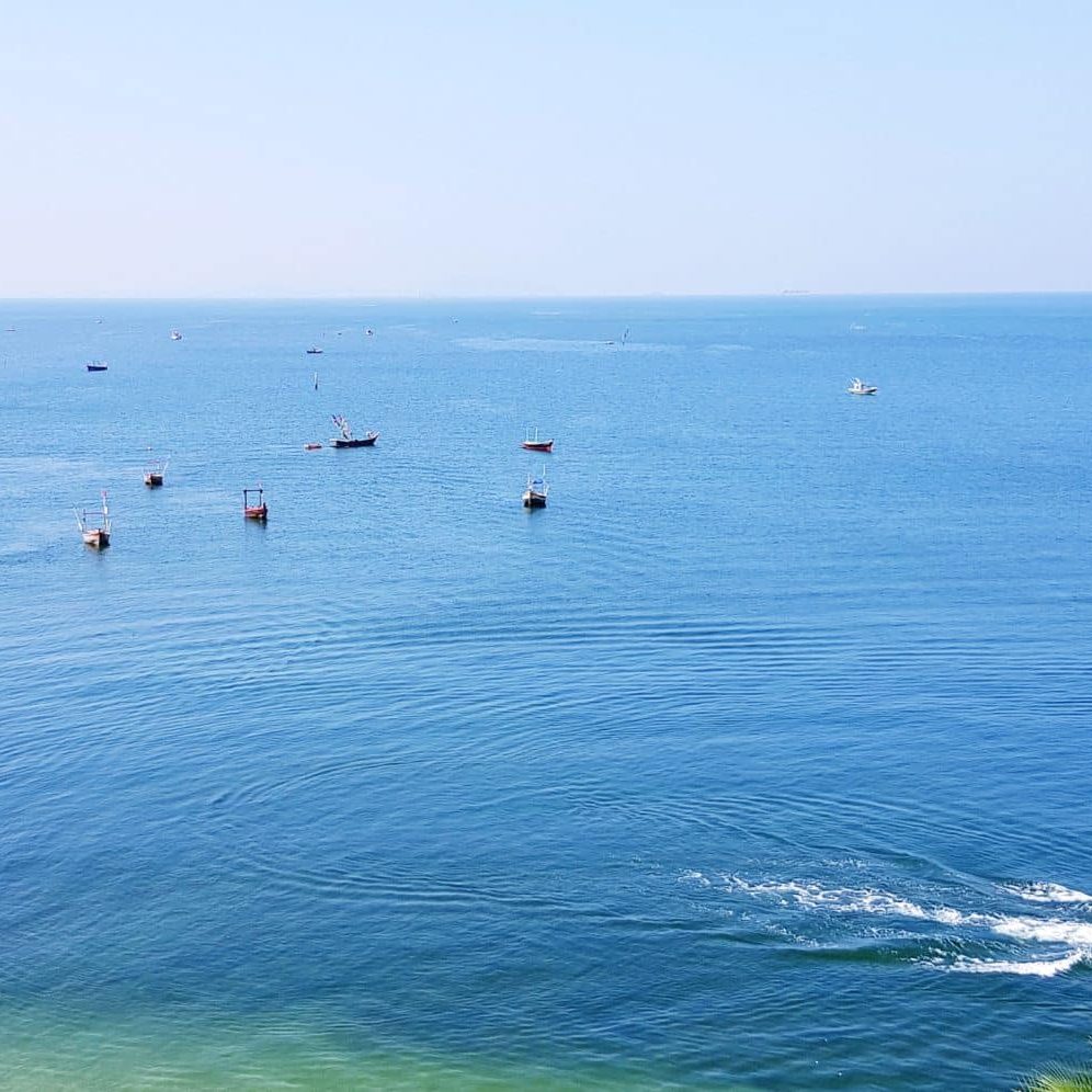 Several boats float on a calm blue Michigan sea under a clear sky, with two people riding a jet ski near the shoreline.