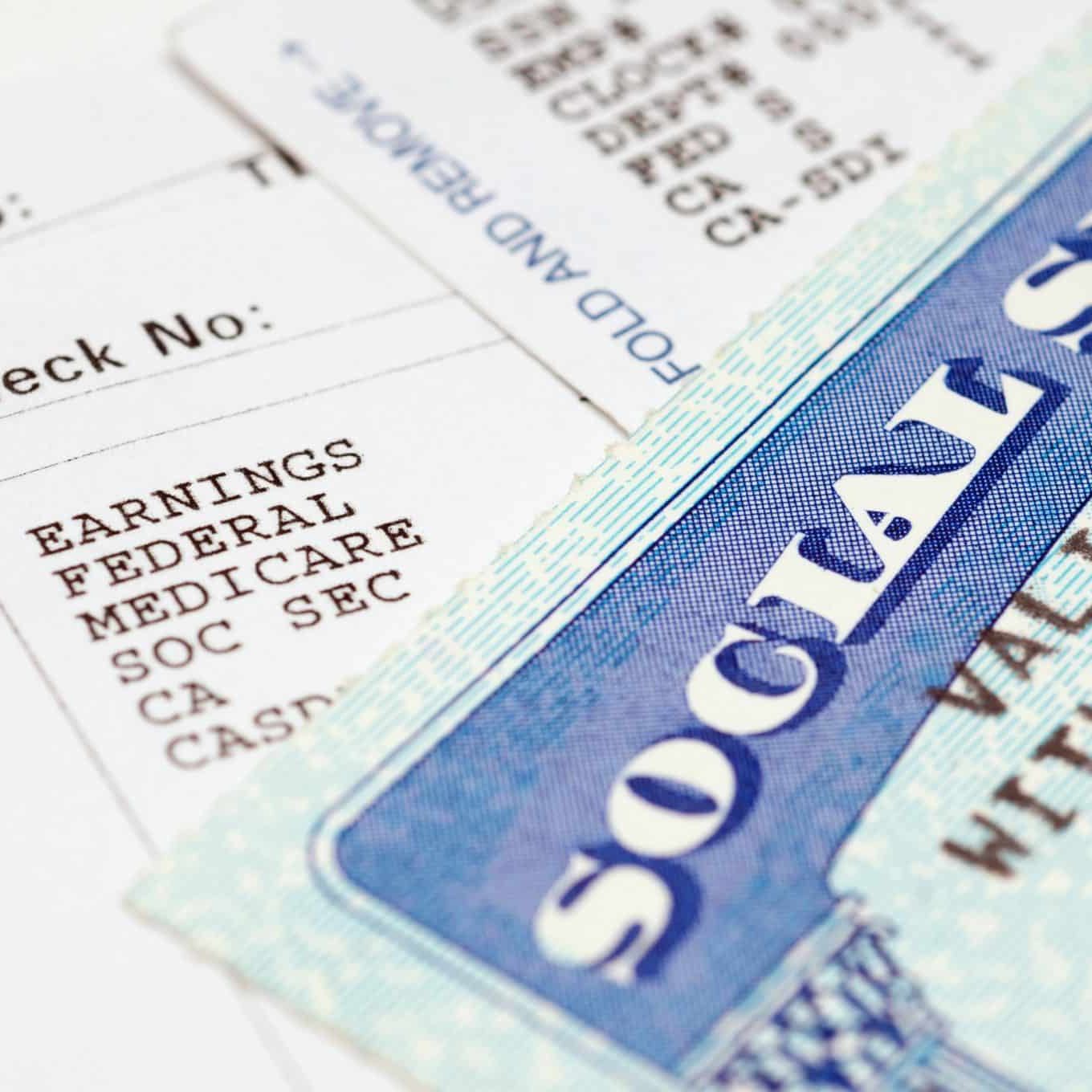 Close-up of a Social Security card partially covering a pay stub listing earnings, federal tax, Medicare, and deductions—capturing the reality many in Lansing face when Social Security claims are denied.