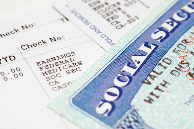 Close-up of a Social Security card partially covering a pay stub listing earnings, federal tax, Medicare, and deductions—capturing the reality many in Lansing face when Social Security claims are denied.