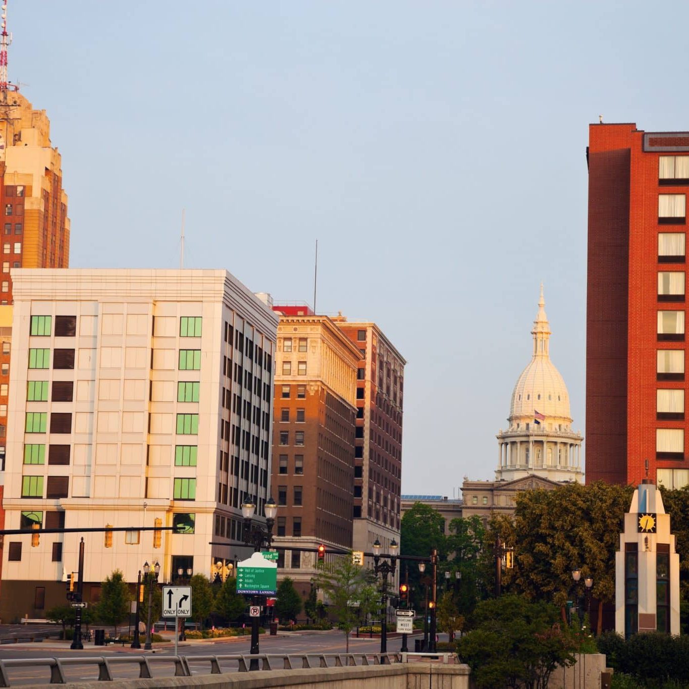 Downtown cityscape with several buildings, including a clock tower and a domed capitol building in the background, under a clear sky.