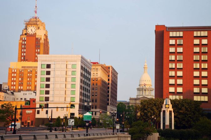 Downtown cityscape with several buildings, including a clock tower and a domed capitol building in the background, under a clear sky.