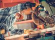 A person wearing gloves and a plaid shirt uses a circular saw to cut a wooden board in a workshop.