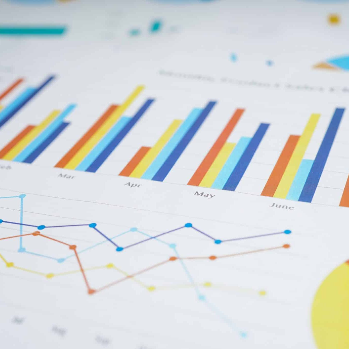 A close-up of printed charts showing colorful bar graphs, line graphs, and pie charts with monthly data on white paper.