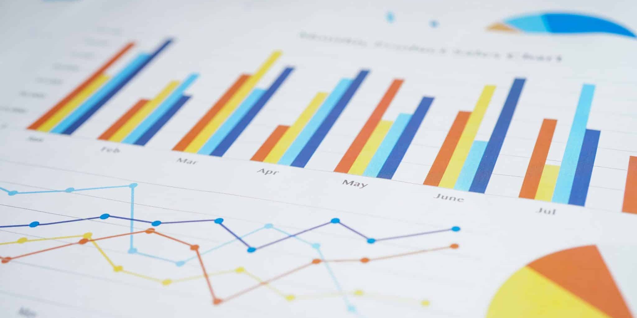 A close-up of printed charts showing colorful bar graphs, line graphs, and pie charts with monthly data on white paper.
