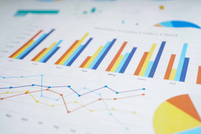 A close-up of printed charts showing colorful bar graphs, line graphs, and pie charts with monthly data on white paper.