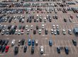 Aerial view of a large parking lot with multiple rows of parked cars and some empty spaces, seen on a sunny day.