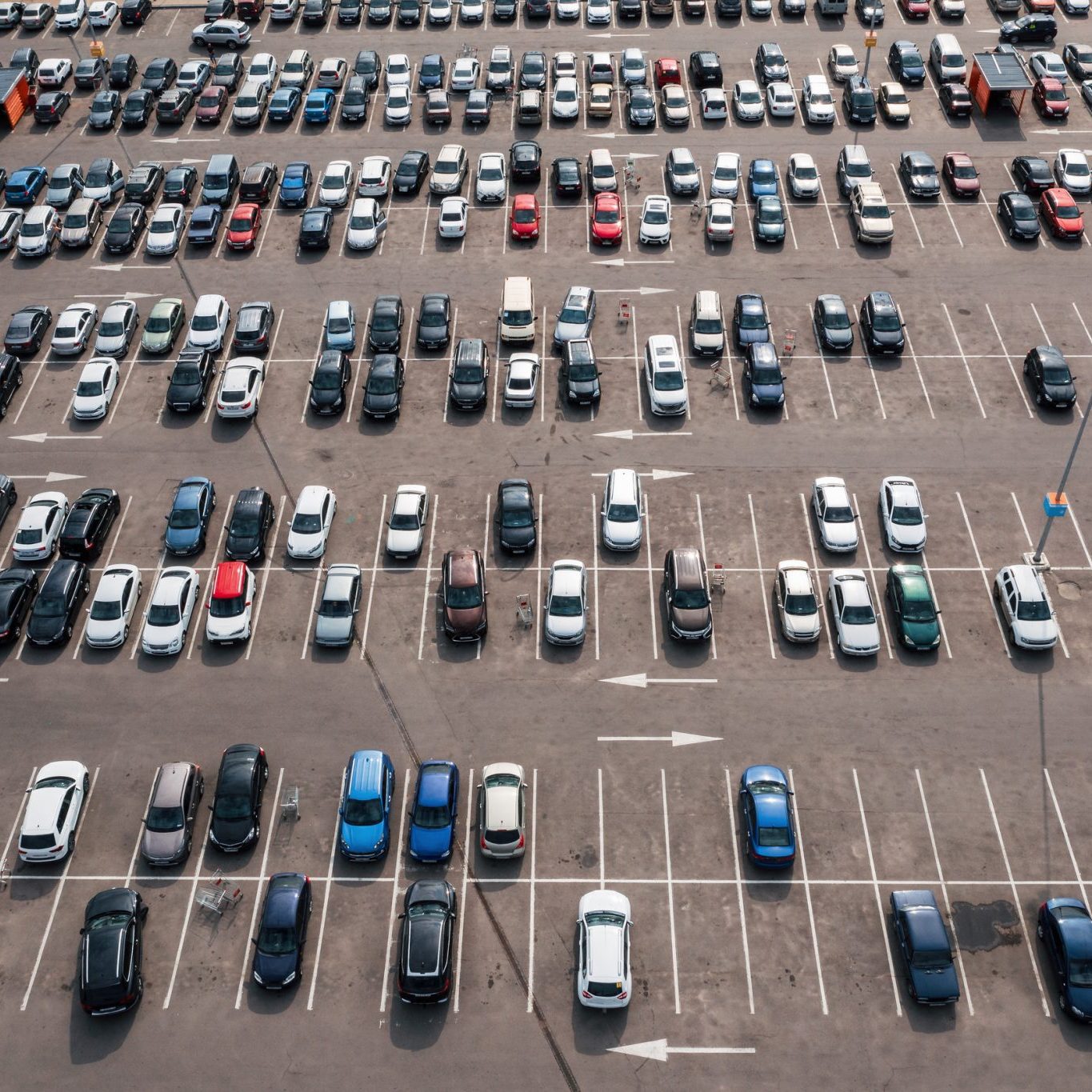 Aerial view of a large parking lot with multiple rows of parked cars and some empty spaces, seen on a sunny day.