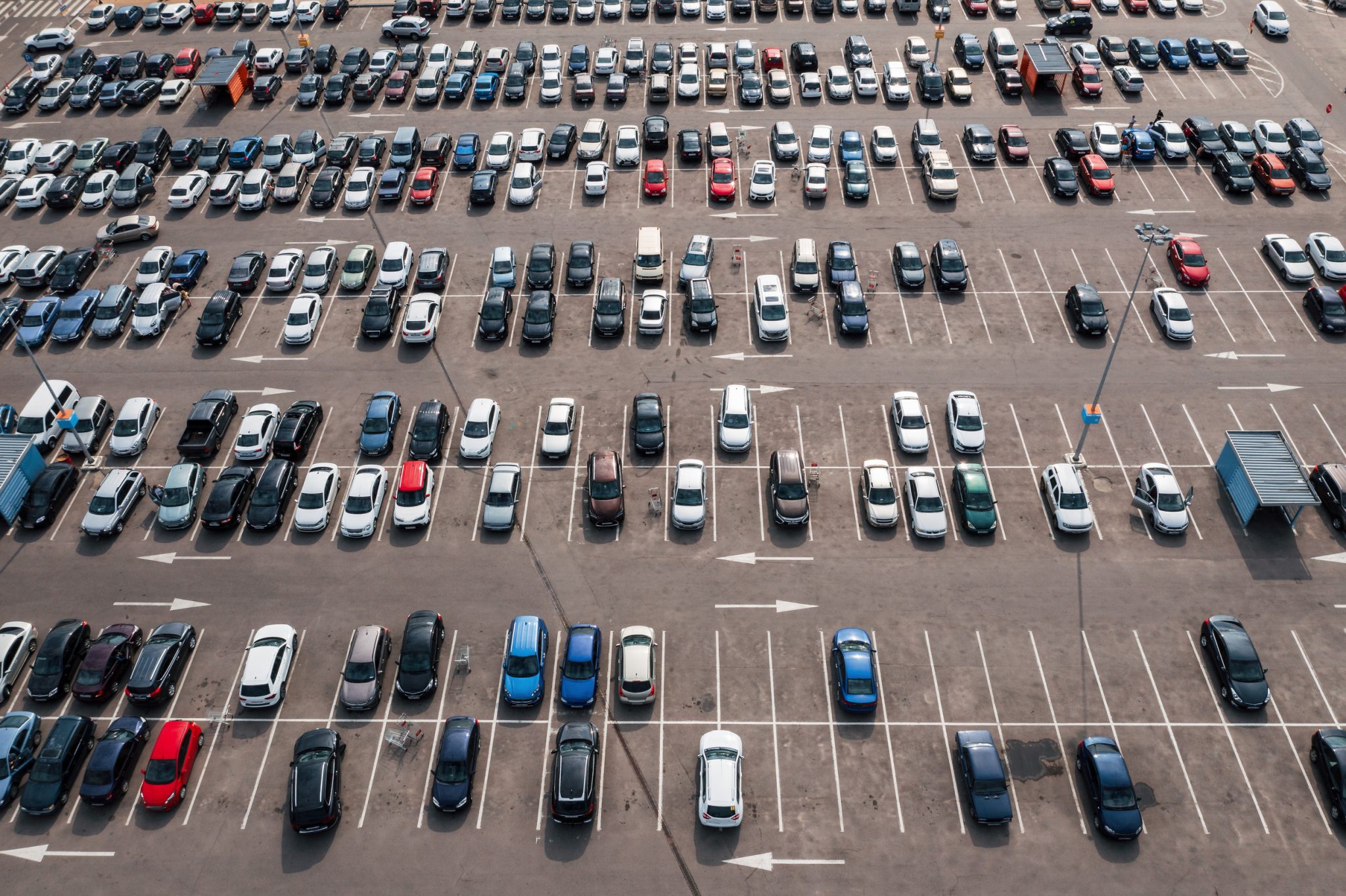 Aerial view of a large parking lot with multiple rows of parked cars and some empty spaces, seen on a sunny day.