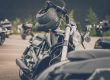 A black motorcycle parked in a lot with other bikes, featuring a black helmet resting on its handlebars.