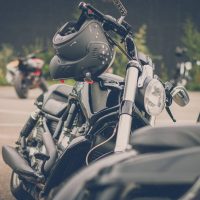 A black motorcycle parked in a lot with other bikes, featuring a black helmet resting on its handlebars.