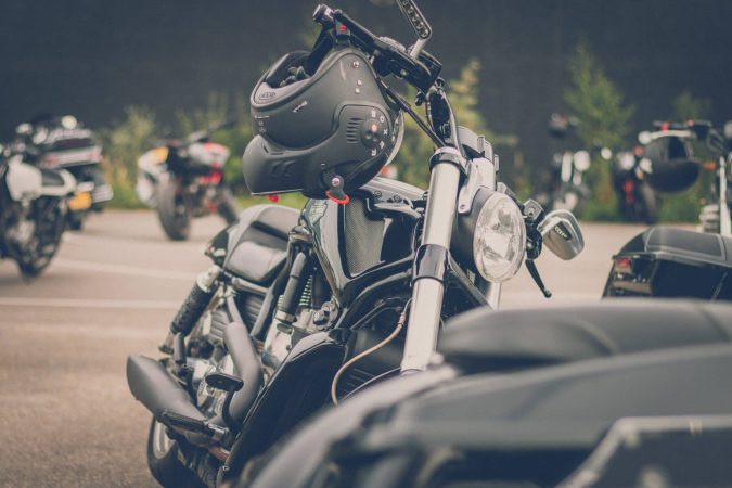 A black motorcycle parked in a lot with other bikes, featuring a black helmet resting on its handlebars.