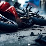 A red motorcycle lies damaged on the road surrounded by debris, indicating a recent accident.