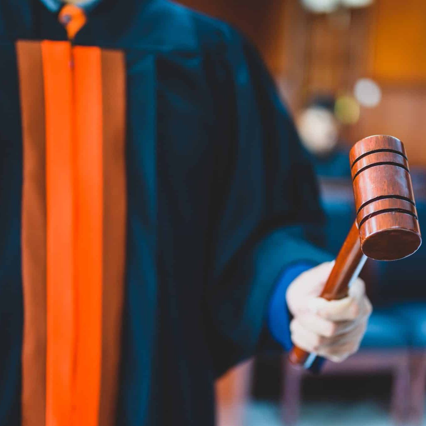 A person in a judge’s robe holds a wooden gavel in a courtroom setting.