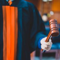 A person in a judge’s robe holds a wooden gavel in a courtroom setting.