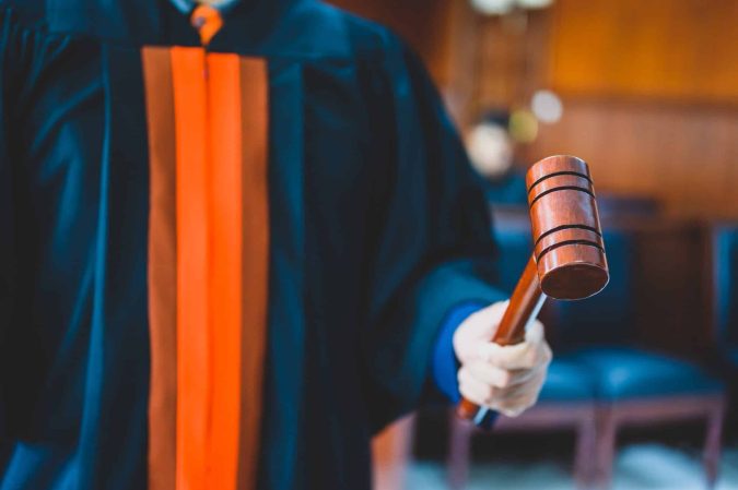 A person in a judge’s robe holds a wooden gavel in a courtroom setting.