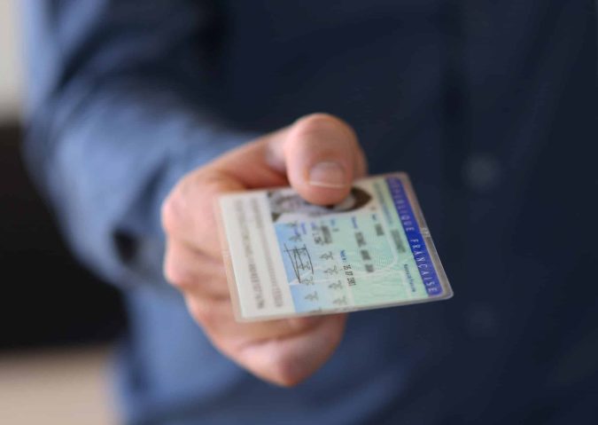 A person in a blue shirt holds out a French identification card, showing the front side with text and a photo visible.