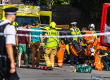 Emergency responders assist several people at the scene of an incident on a city street, with a fire truck and ambulance visible in the background.