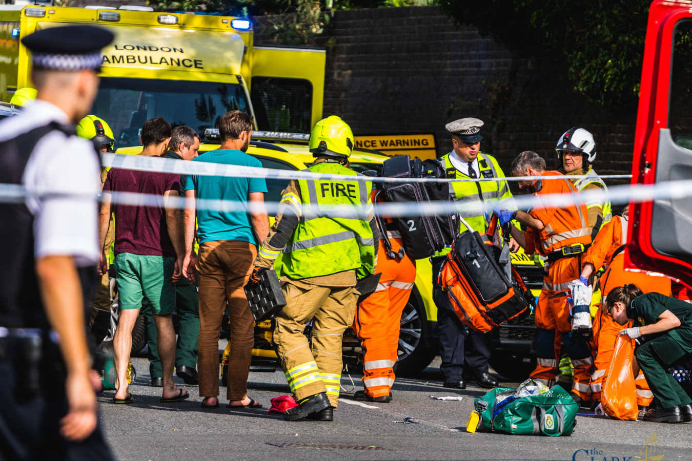 Emergency responders assist several people at the scene of an incident on a city street, with a fire truck and ambulance visible in the background.