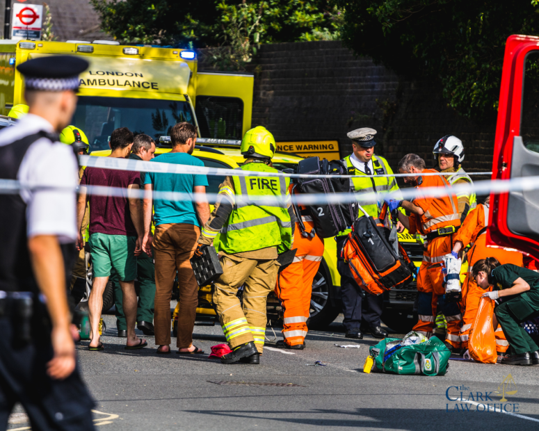 Emergency responders assist several people at the scene of an incident on a city street, with a fire truck and ambulance visible in the background.