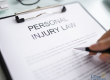 A clipboard holds a document titled "Personal Injury Law" with a hand holding a pen hovering over the paper; The Clark Law Office logo appears in the bottom right corner.